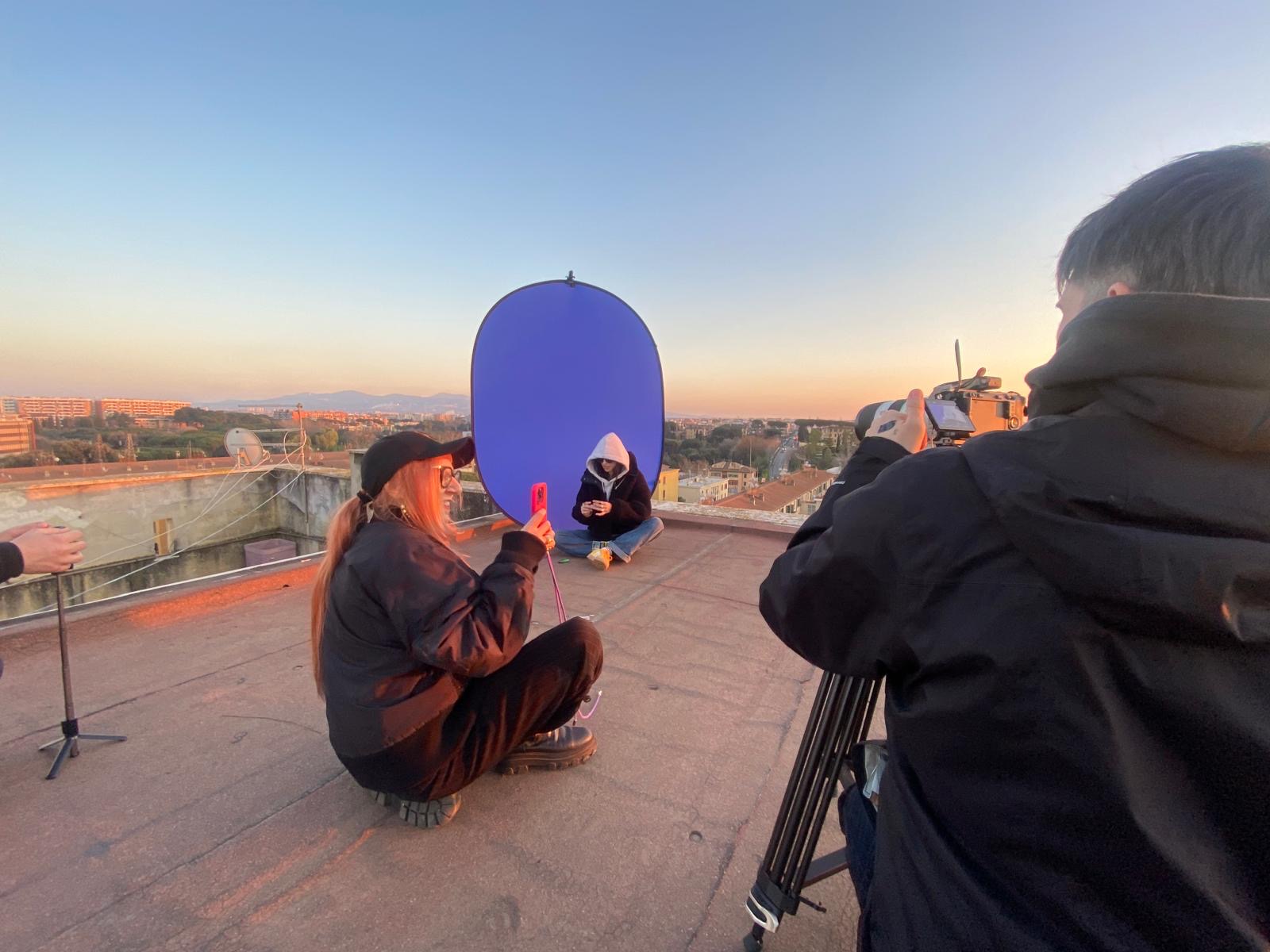 tre persone su un terrazzo utilizzano macchine fotografiche e telefoni per fare delle riprese.