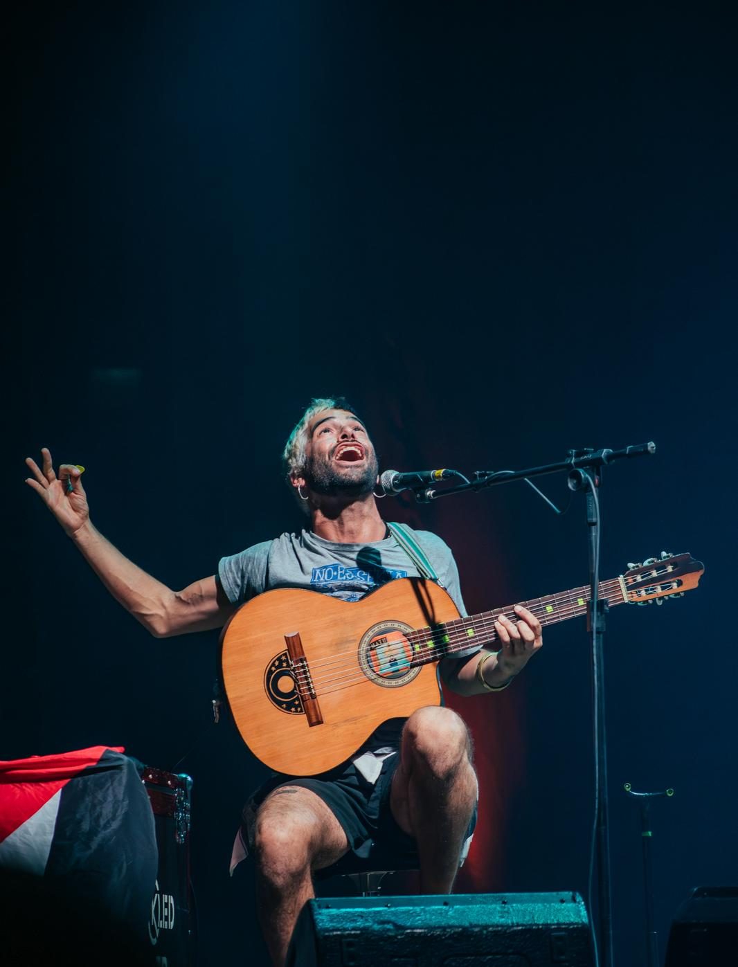 performer canta seduto su un palco con la chitarra e lo sguardo rivolto verso l'alto